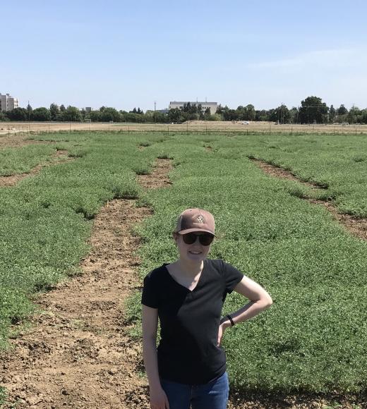 Claire Spickermann standing in a field with rows of short plants extending behind her.